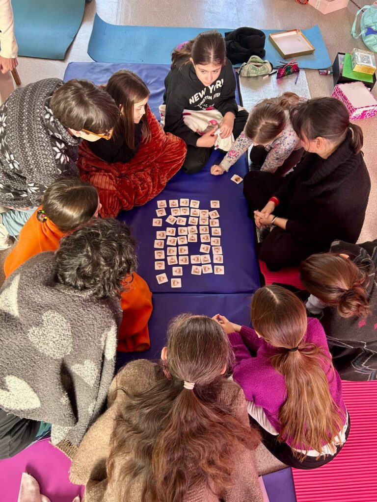 Educatrice che guida un laboratorio della Fata del Grembo con bambine e mamme, in un ambiente interattivo e accogliente."