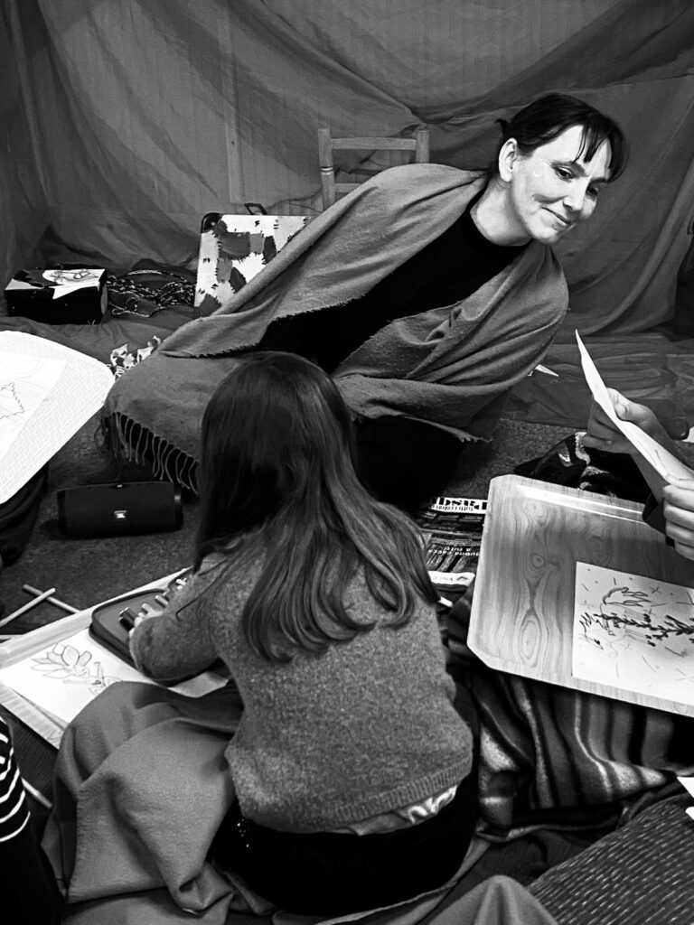 Educatrice che guida un laboratorio della Fata del Grembo con bambine e mamme, in un ambiente interattivo e accogliente."